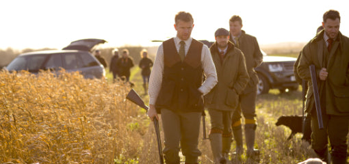 Hunters in traditional attire walking through a golden field at sunrise during the Glorious Twelfth, the start of the grouse shooting season. Ideal for those seeking classic British hunting experiences.