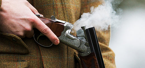 Person in a tweed jacket, breaking open a smoking Purdey shotgun after firing.