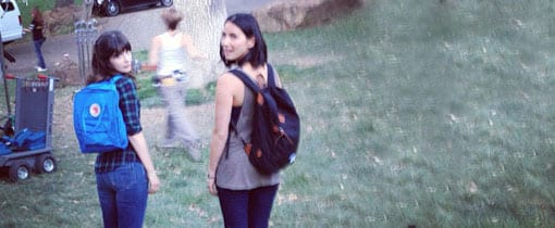 Zooey Deschanel pictured with Olivia Munn on the set of New Girl, both wearing backpacks. Zooey sports an Ice Blue Fjällräven Kanken Classic, a popular choice for stylish and functional gear.