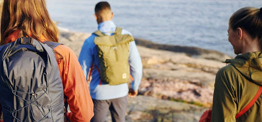People walking along a rocky coastline, wearing backpacks and outdoor apparel.