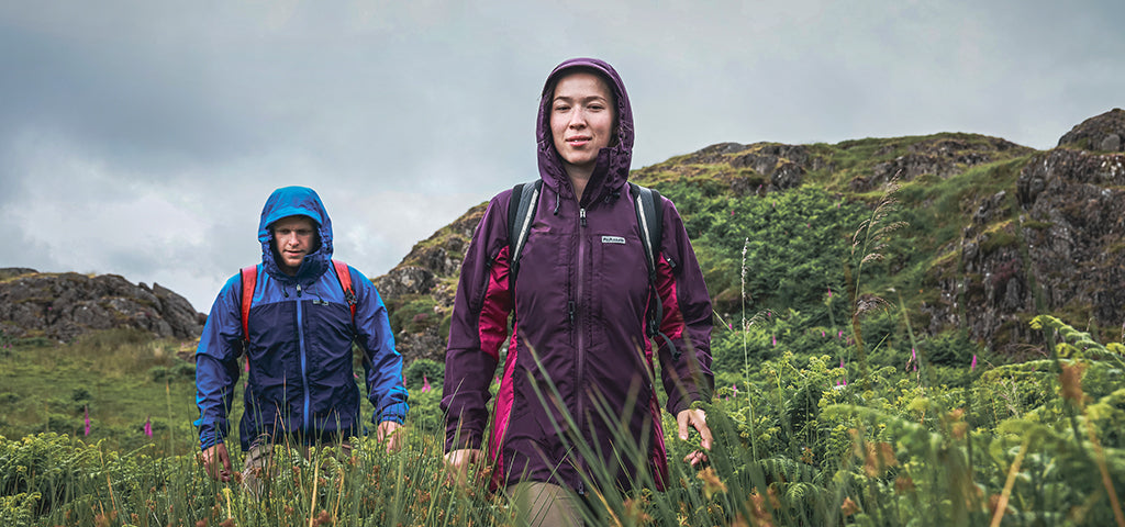 Two hikers wearing Paramo jackets trekking through a lush, mountainous landscape.