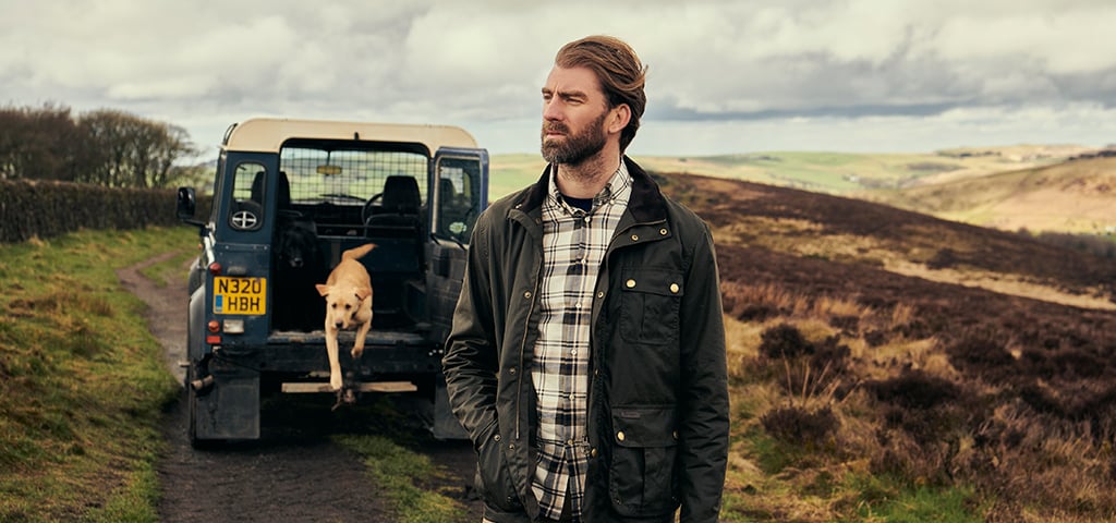 Man Wearing Classic Barbour Jacket standing next to Landrover