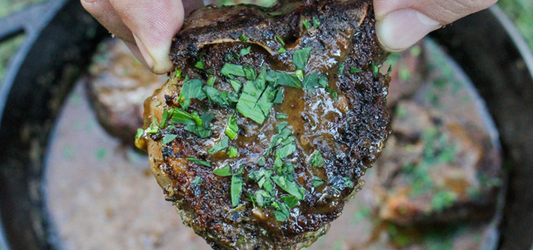 Delicious grilled lamb chop garnished with fresh herbs, held above a skillet. Perfectly cooked and seasoned for a mouth-watering meal.