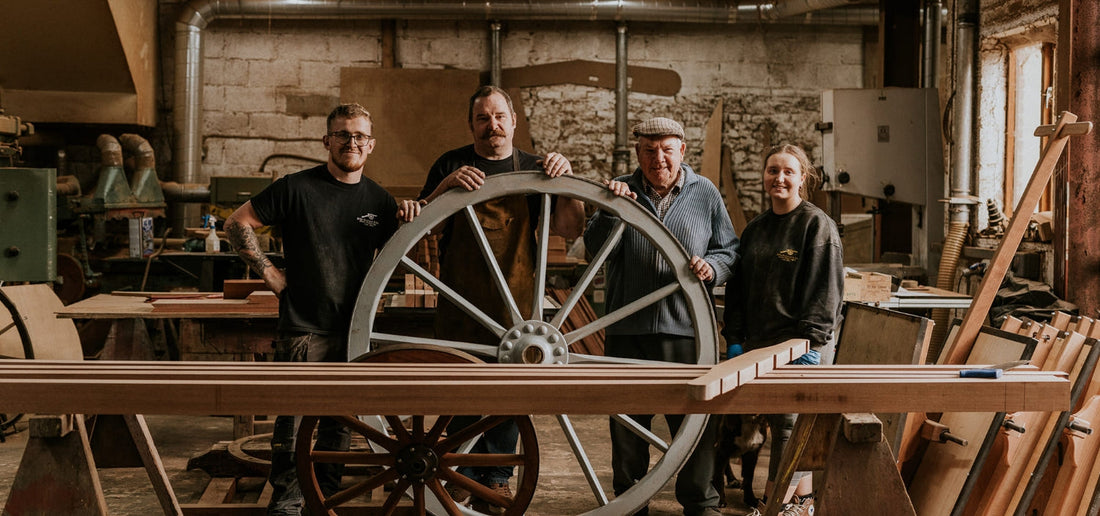 Four wheelwrights in a Devon workshop standing behind a large traditional wooden cart wheel in restoration