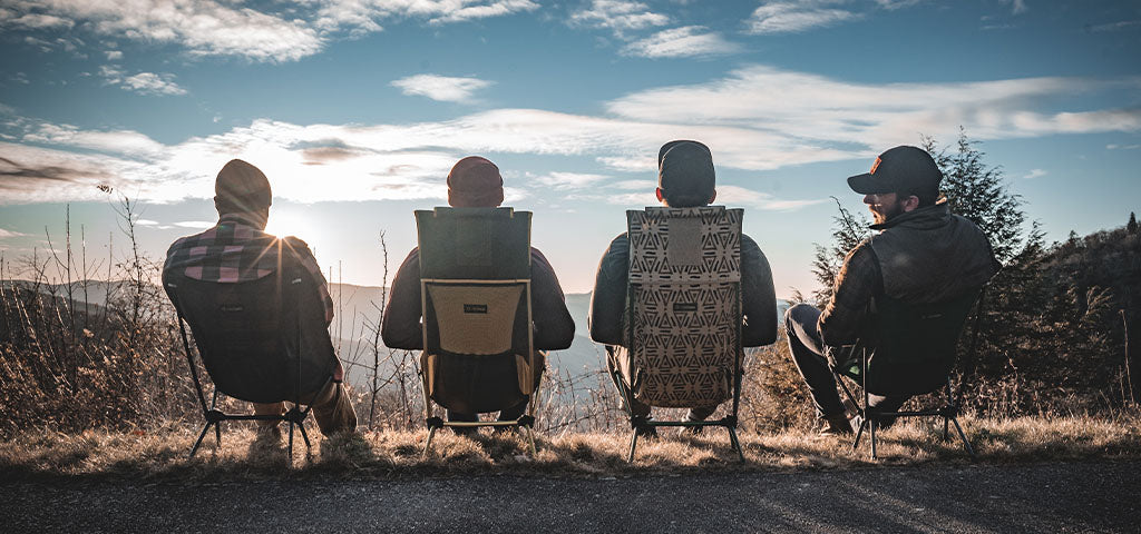 Helinox camping chairs in use, featuring four people sitting and enjoying a scenic mountain view at sunset. Lightweight and durable outdoor seating perfect for hikers and campers.