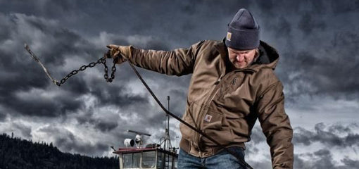 Carhartt WIP rugged workwear, featuring a man in a brown jacket and beanie working with chains. Durable and reliable clothing designed for tough outdoor conditions.