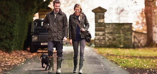 Couple wearing Barbour Clothing walking down drive with dog on Country Estate