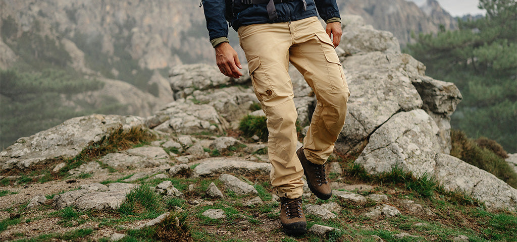A person hiking in the mountains wearing Fjallraven trousers and brown hiking boots.