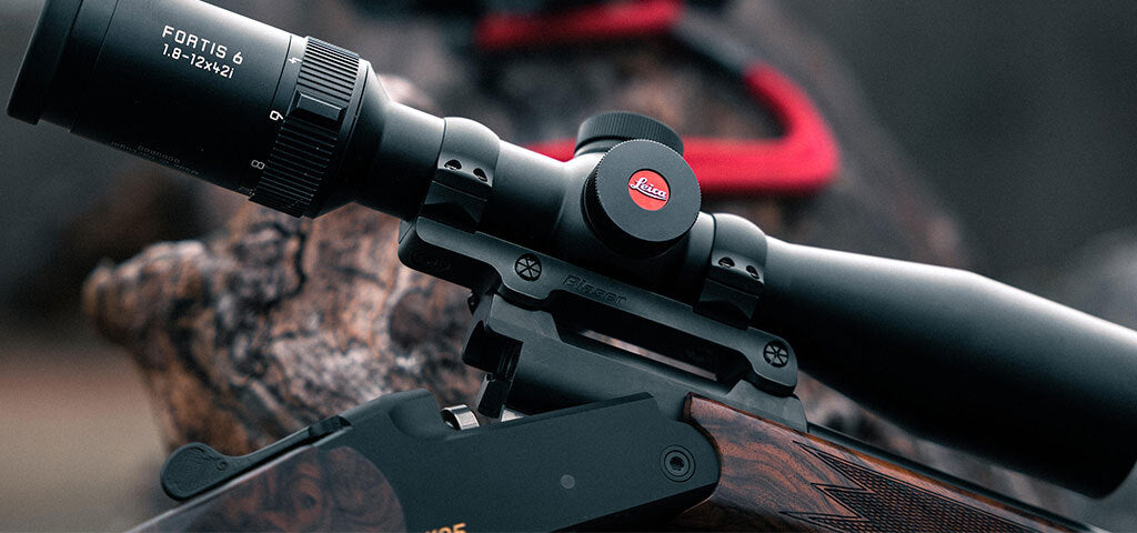 Close-up of a rifle with a Leica Fortis 6 scope mounted on top, set against a blurred natural background.