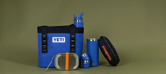 Blue YETI cool bag with matching bottle, tumbler and food container alongside a Patagonia zip case on a plain studio background.