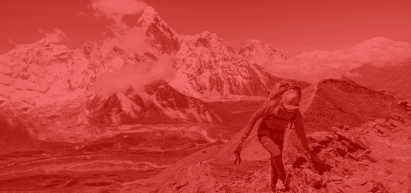 Woman wearing Patagonia Climbing Gear and Backpack, walking through a mountain trail with snow-capped peaks in the background, photo has a red filter.
