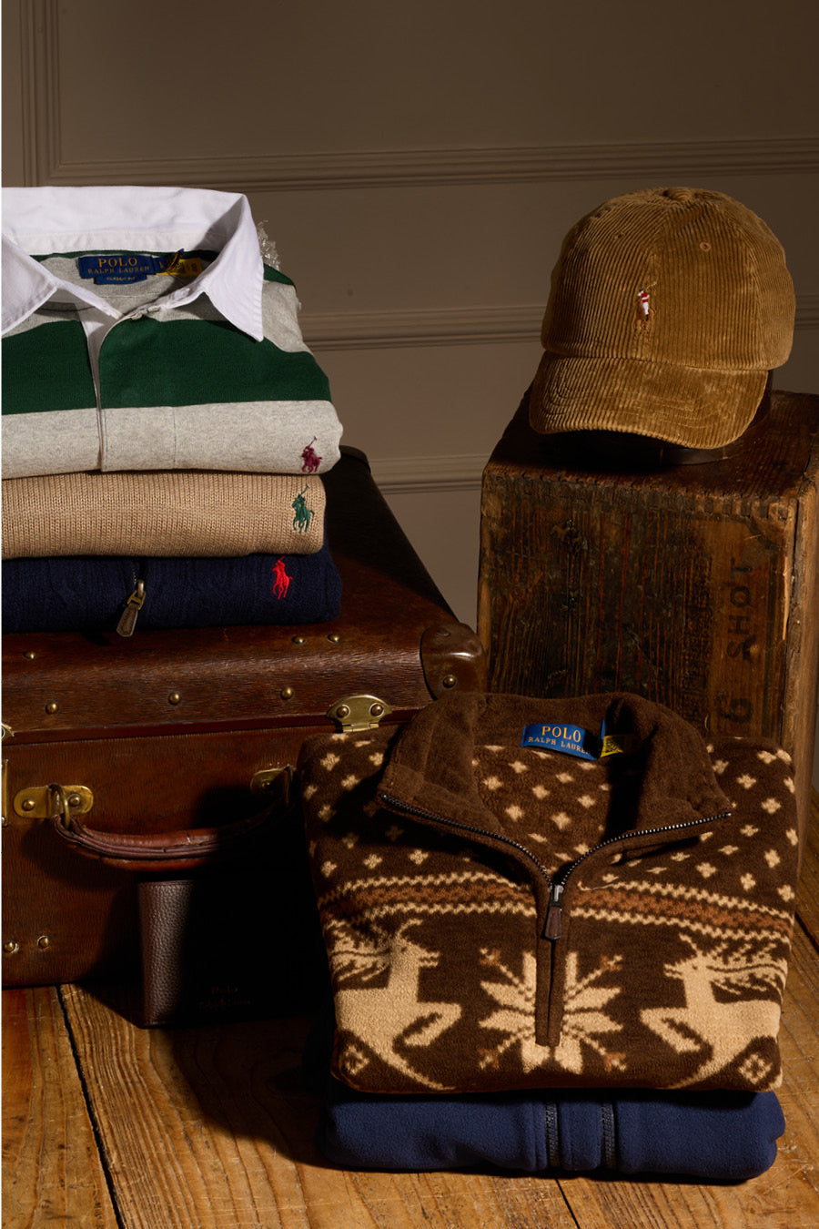 Stack of Polo Ralph Lauren clothing items including a jacket, shirt, and cap on a wooden surface with a brown background.