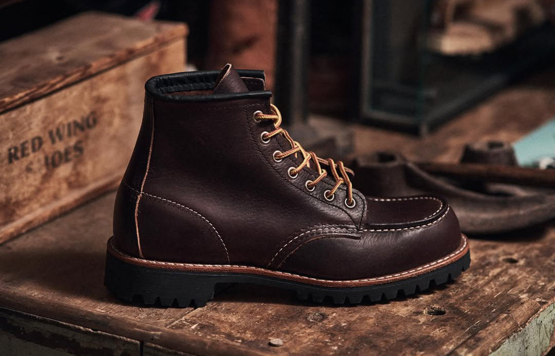 Brown leather Red Wing boot with tan laces on a wooden surface next to a Red Wing box.