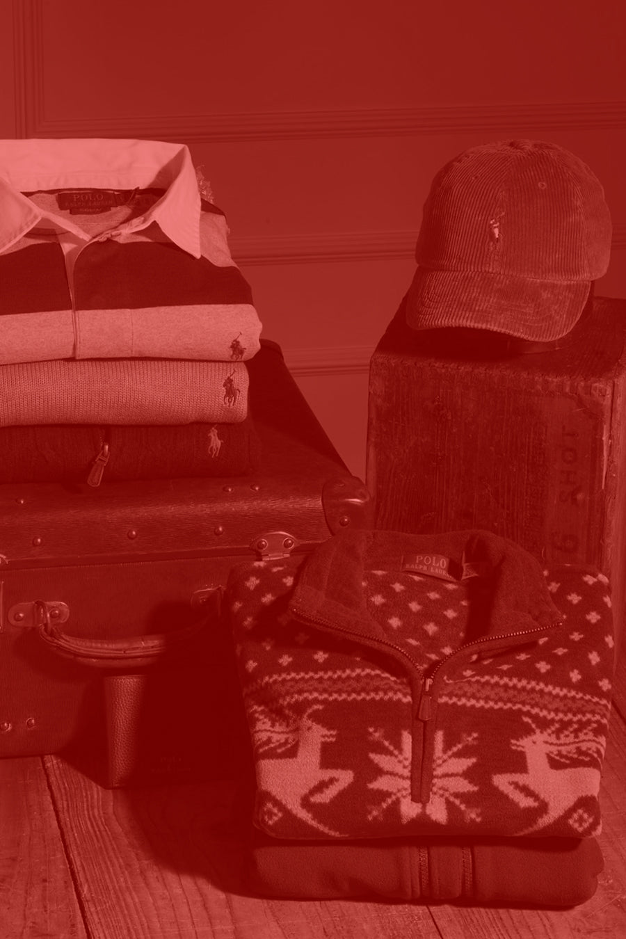 Stack of folded Polo Ralph Lauren clothes, a suitcase, and a cap on a wooden surface with a red filter.