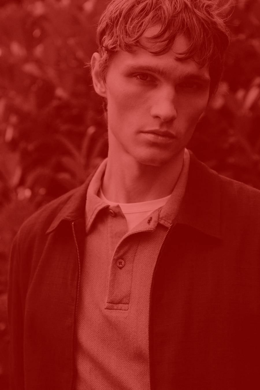 Man wearing a dark Sunspel coat over a light shirt with a blurred natural background