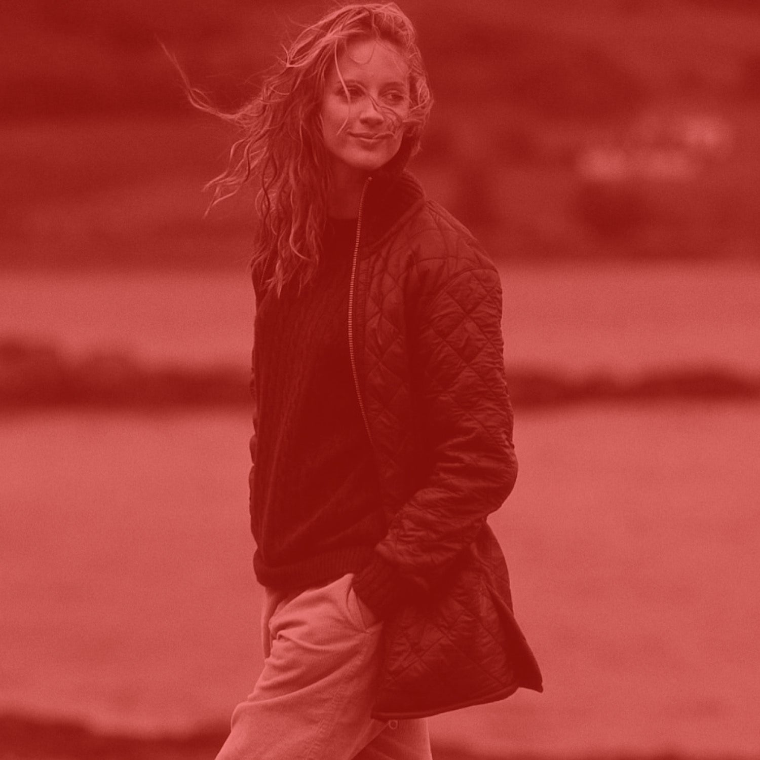 Woman wearing a dark quilted jacket in a field with a red filter